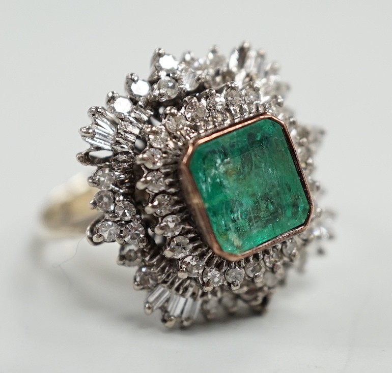 A white metal and single stone emerald set dress ring, bordered with two stepped bands of round and baguette cut diamonds, size K, gross weight 7.6 grams.